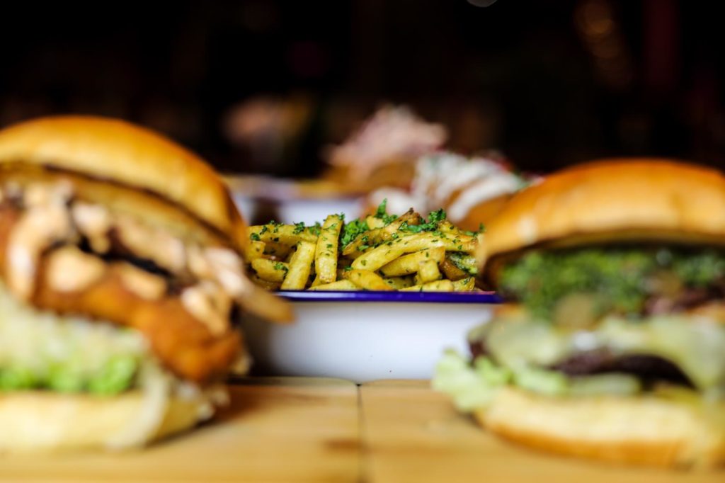 photo of two burgers slightly blurred in foreground, with bowl of fries in focus in background