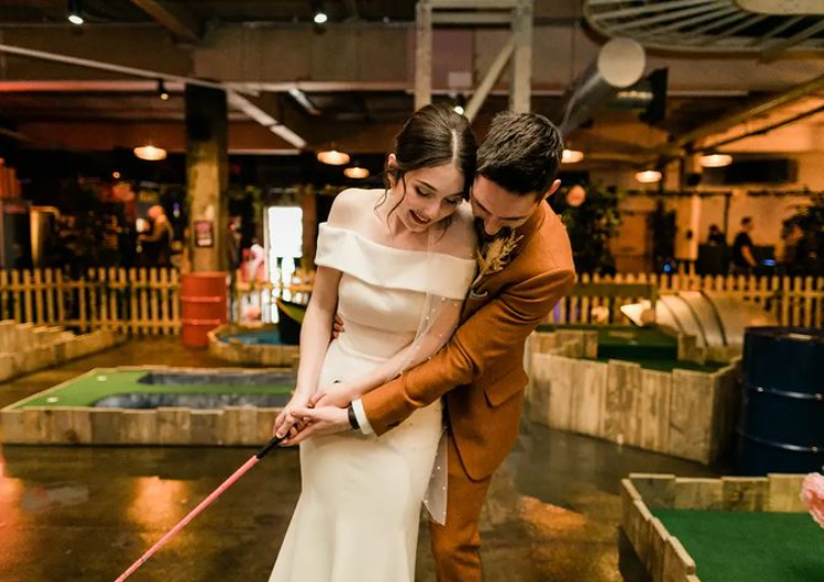 bride in wedding dress and groom in suit getting married at Fore Play Crazy Golf swinging golf club